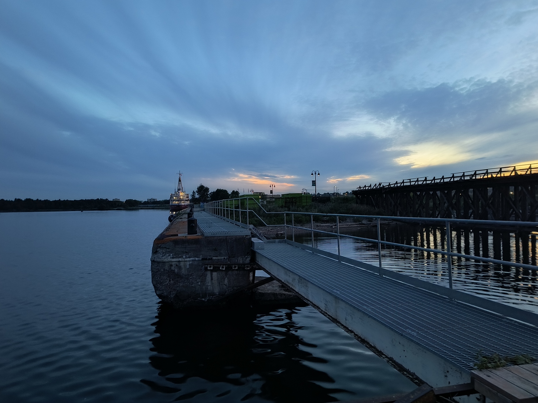 a photo of a dock with a boat on the left side during sundown