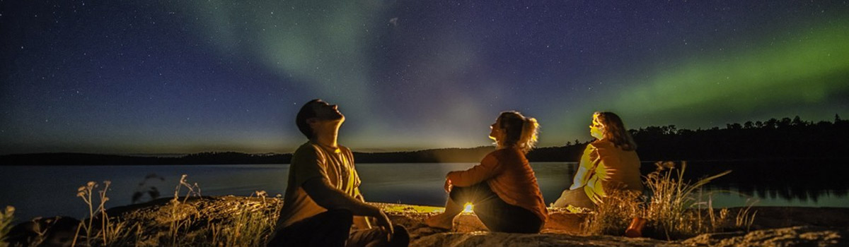 people looking up at the northern lights in a by a fire