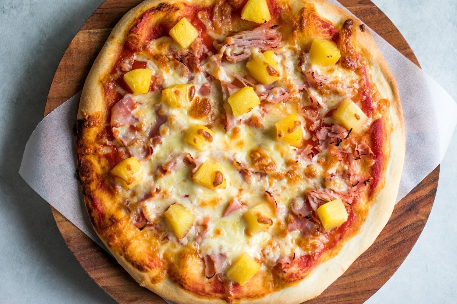 a top down photo of a hawaiian pizza on a cutting board